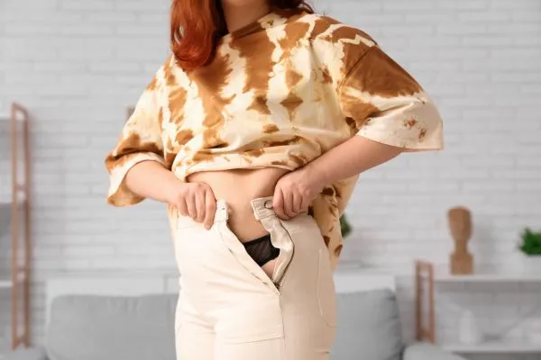 Image of woman trying to do her trousers up after pregnancy weight gain Hickstead
